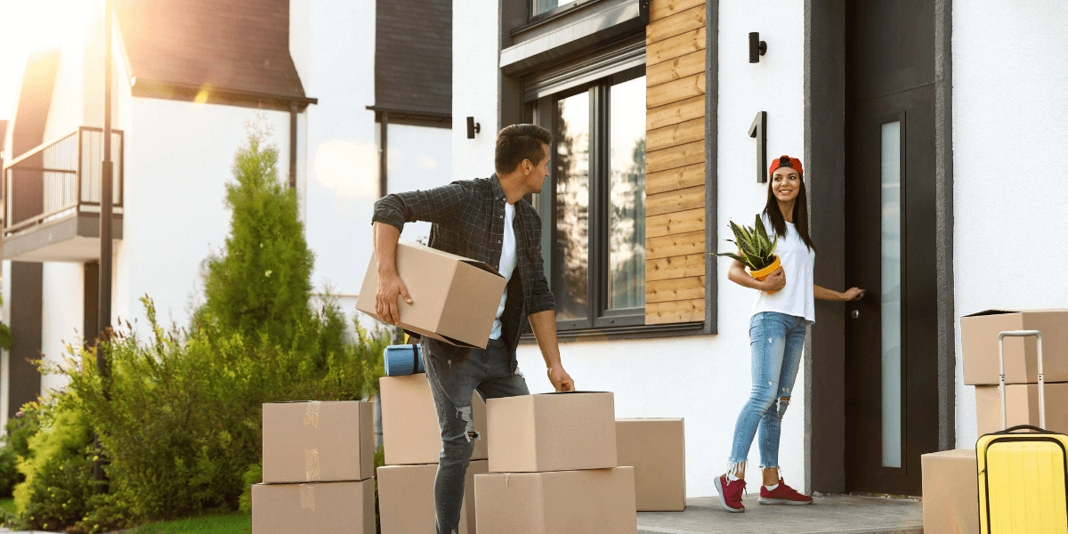 A man and woman carrying boxes into a house, preparing for a move.