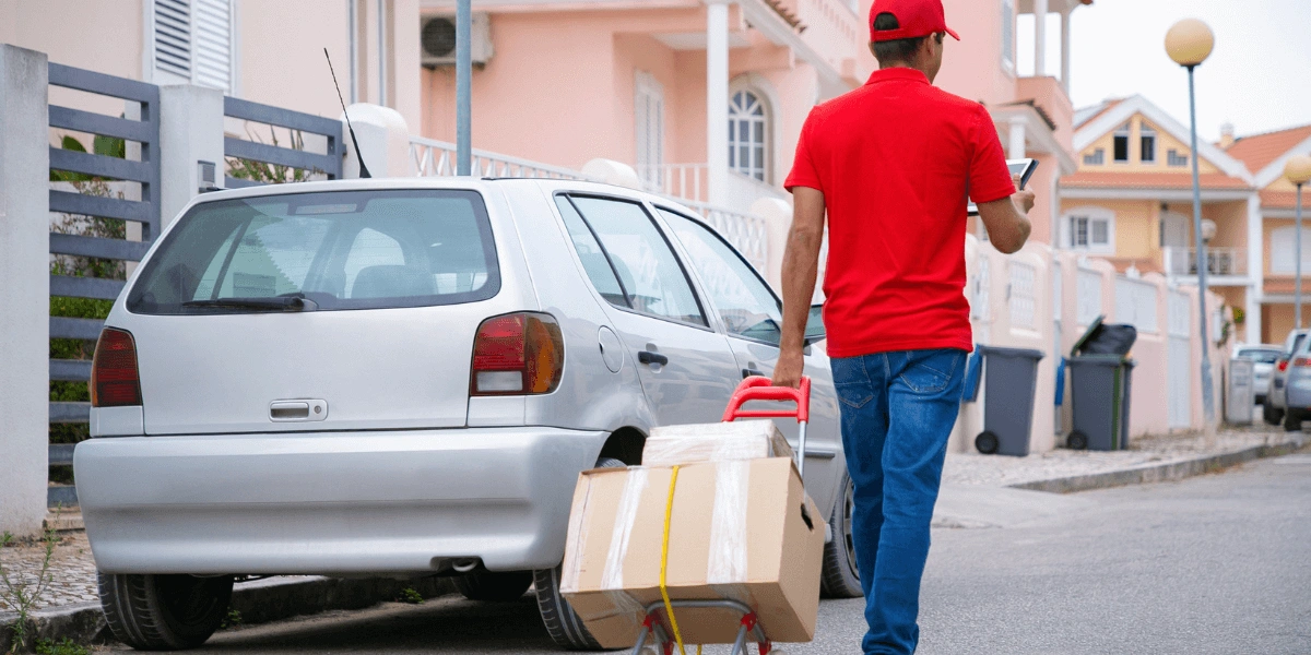 A man in a red shirt carries a box and a toy car, showcasing a playful and busy moment.